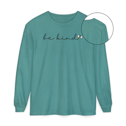 On the front of this custom unisex long sleeve shirt are the words be kind in a simple cursive font, with a bumble bee on the right side of the letter kind, on the back right shoulder there is an image of a bumble bee flying and leaving a trail behind it in the shape of a heart.