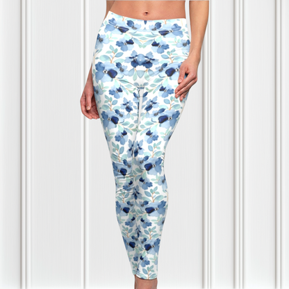 A pair of custom handmade high waisted women's leggings that are white and have a blue floral pattern with green leaves all over the pants.