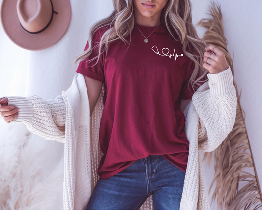 On the front of this custom health care workers shirt, on the left chest of the top is a stethoscope that has a heart and a heartbeat in the cord of the stethoscope.