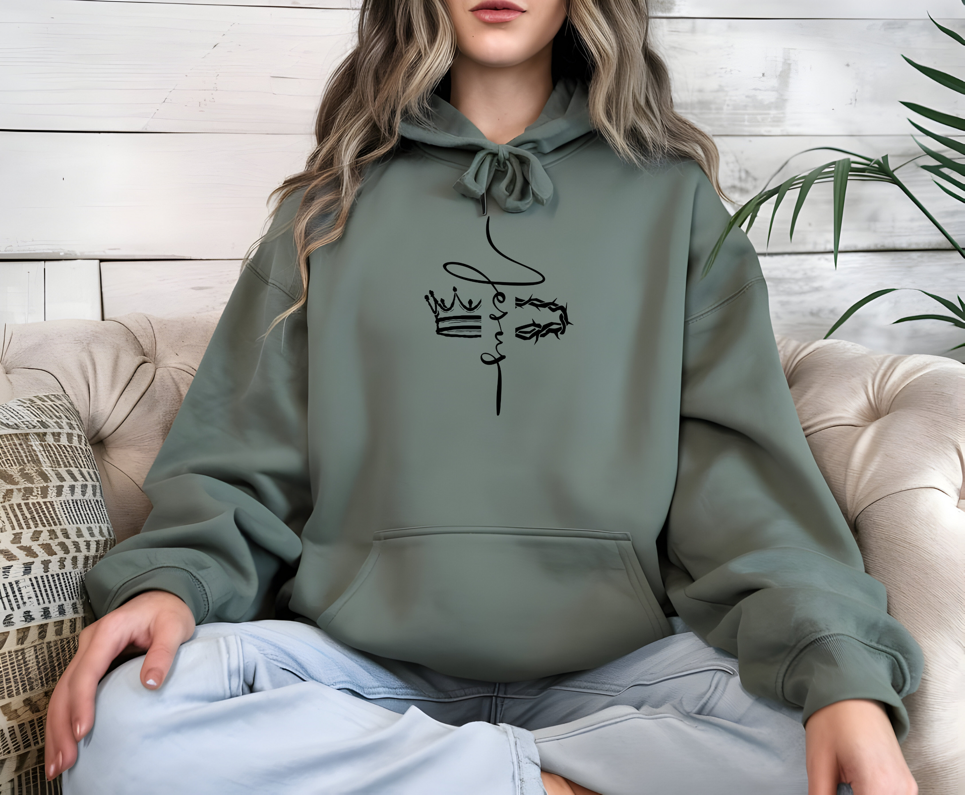 This custom unisex Christian hoodie features the name of Jesus in a cursive font down the center of the front of the sweater, there is an image of a crown on the right and a crown of thorns on the left of the name of Jesus.