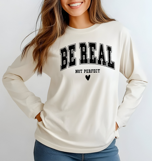 On the front of this custom unisex long sleeve shirt are the words Be Real in large bubble font with the words not perfect underneath the bubble letters, on the bottom there is a heart.