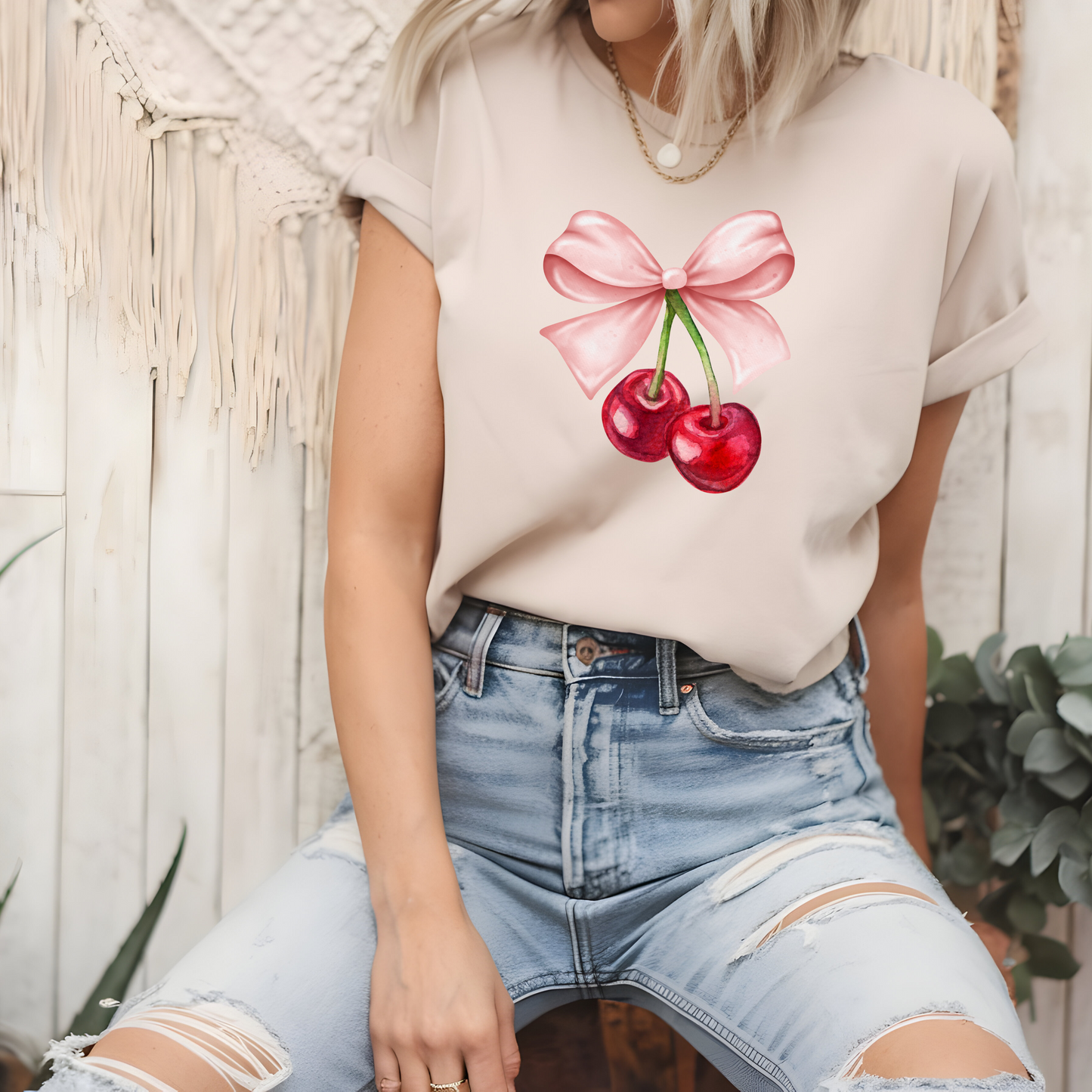On the front of this custom women's short sleeve shirt is an image of a pair of cherries hanging from a stem with a pink bow on the top of them.