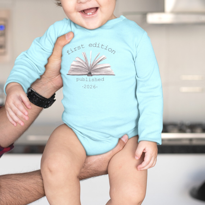 On the front of this custom baby onesie are the words First Edition Published 2026 with an image of an open book in the middle of the wording.