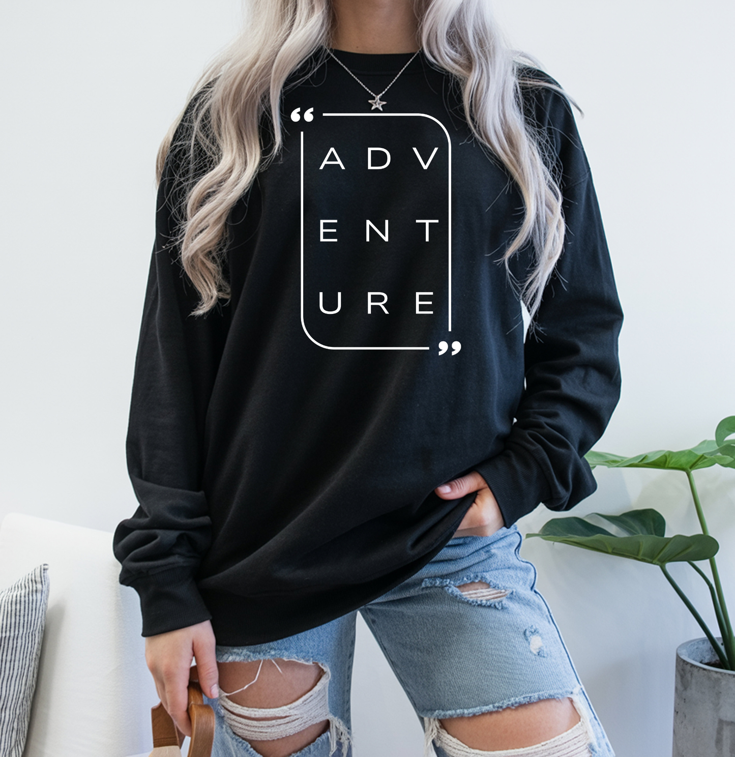 On the front of this super soft unisex long sleeve shirt is the word adventure with there being three letters on each line, it is in a modern font. There is a border around the word.