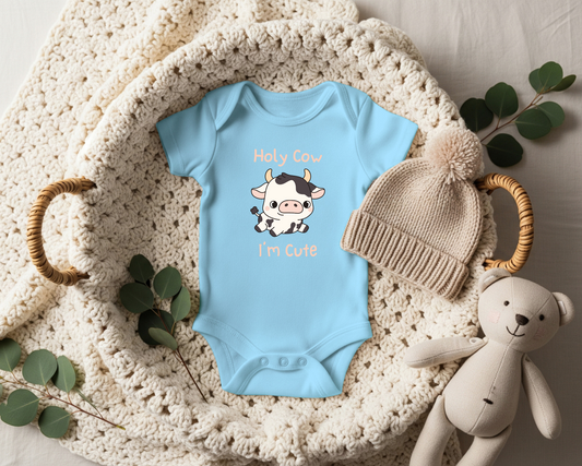 This adorable pink colored super soft bodysuit features an image of a baby cow in the middle with the words 'holy cow I'm cute' in light beige lettering around the image.