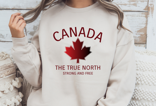 On the front of this custom Canadian pullover sweatshirt is the word Canada in large letters in a half circle overtop of a red and black maple leaf, the words The true north strong and free are underneath the maple leaf, they are also in red.