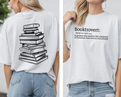 On the front of this custom unisex short sleeve shirt is the word booktrovert with the definition of the word underneath, on the back of the shirt is an image of a large stack of books.