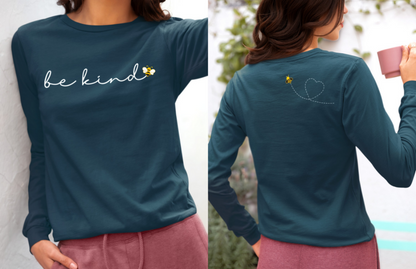 On the front of this custom unisex long sleeve shirt are the words be kind in a simple cursive font, with a bumble bee on the right side of the letter kind, on the back right shoulder there is an image of a bumble bee flying and leaving a trail behind it in the shape of a heart.