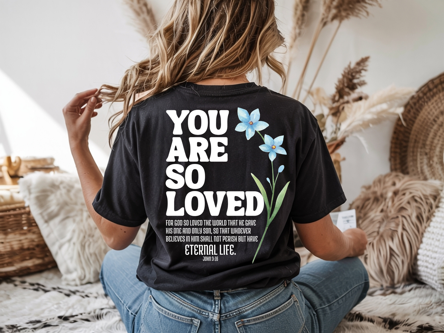 On the back of this Christian custom unisex t-shirt are the words You are loved in large bubble letters with a blue wildflower next to the words, the bible scripture John 3:16 is underneath that reads For God so loved the world that he gave his only son, so that whoever believes in him shall not perish but have everlasting life.