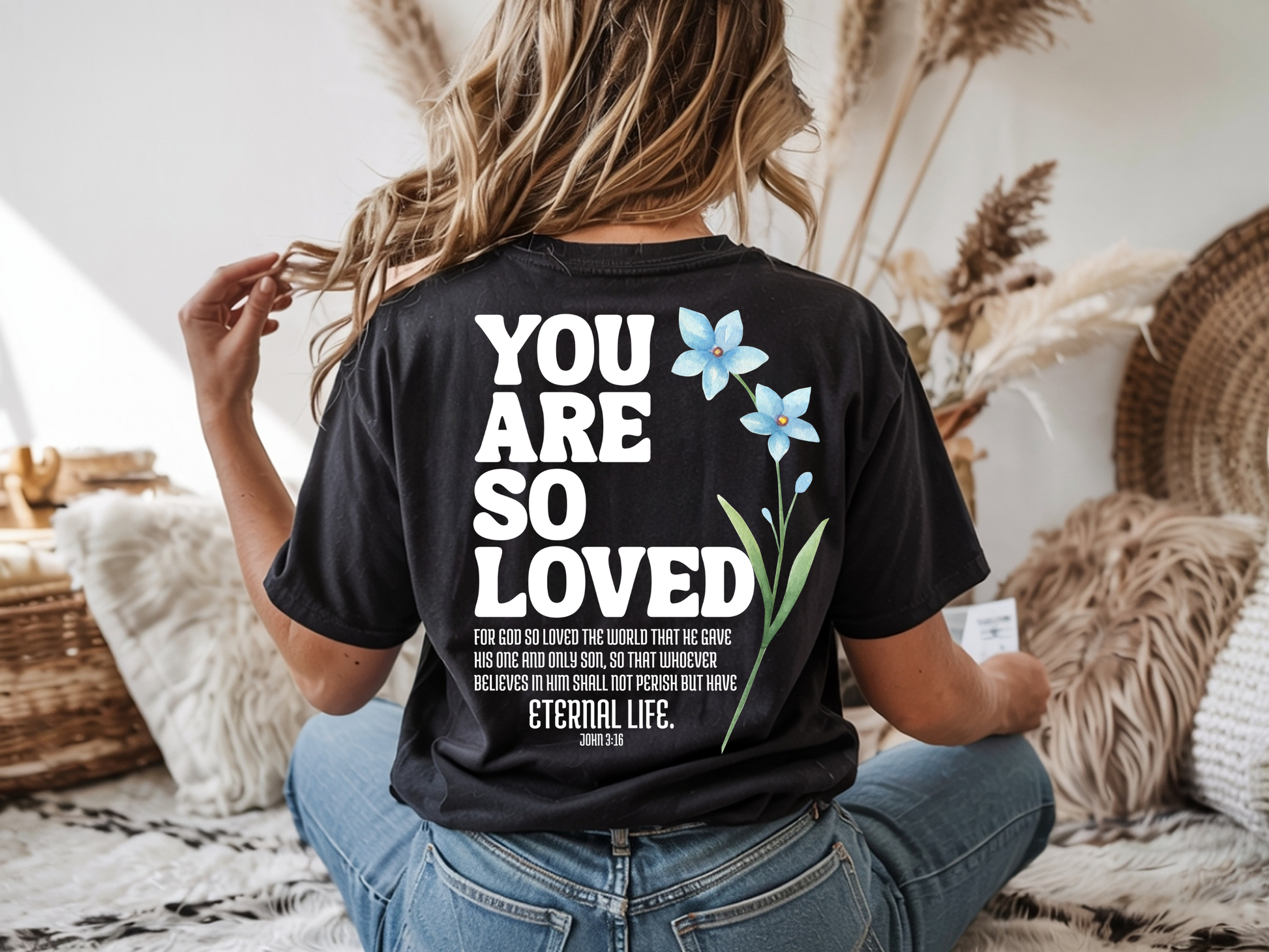 On the back of this Christian custom unisex t-shirt are the words You are loved in large bubble letters with a blue wildflower next to the words, the bible scripture John 3:16 is underneath that reads For God so loved the world that he gave his only son, so that whoever believes in him shall not perish but have everlasting life.