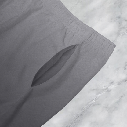 These custom men's board shorts feature a unique design with a ombre pattern starting with a light grey at the top then fading to a dark grey at the bottom, there is a symbol of a dove carrying a fig leaf on the front left side of the shorts just at the knee.