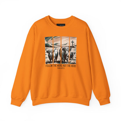 On the front of this Christian pullover sweatshirt is the image of cows standing in a pasture that is in a valley surrounded by mountains, there is a Jesus cross behind the cows, underneath the image is the scripture Follow the word, not the herd Isiah 8:11-13