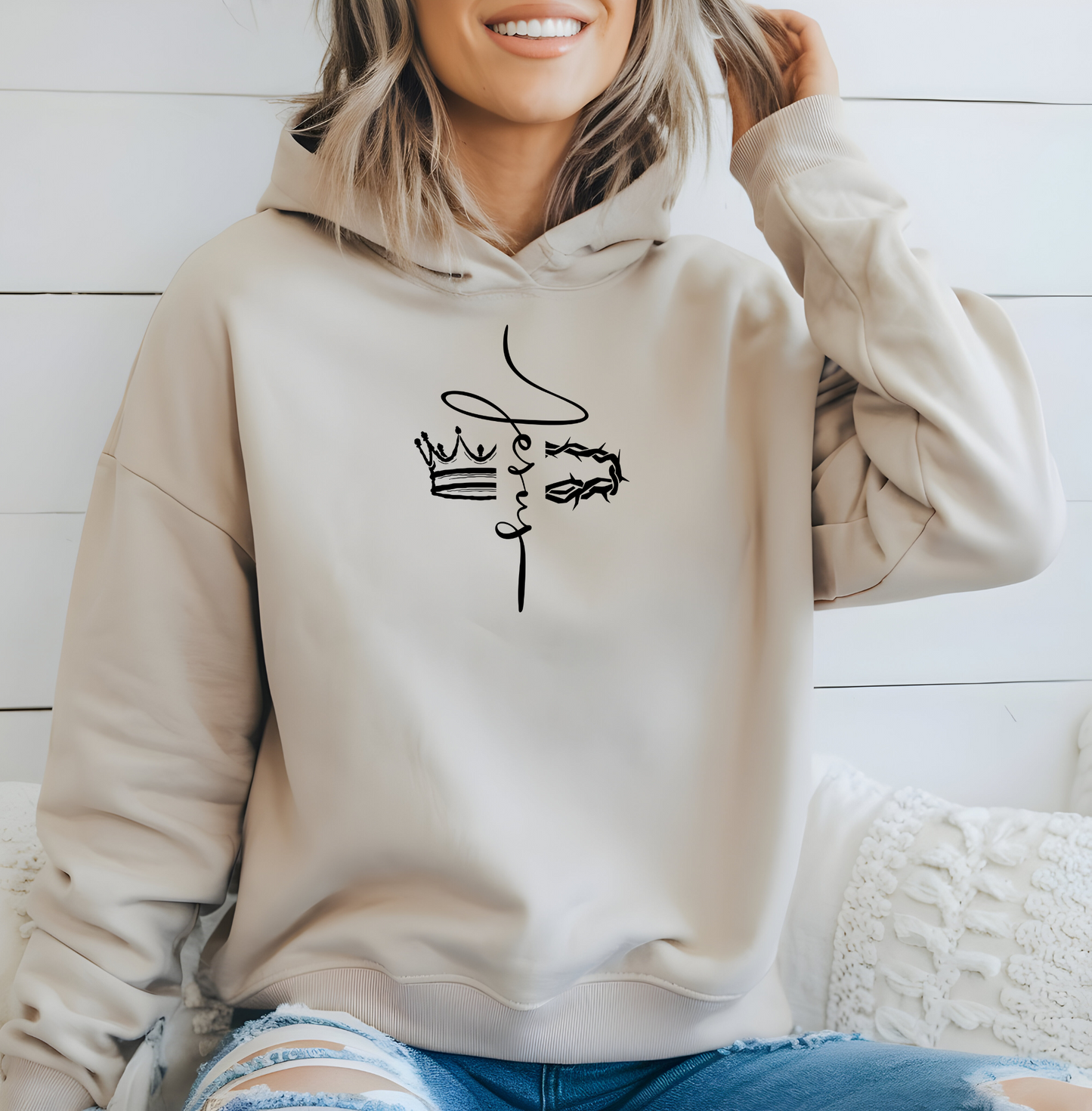 This custom unisex Christian hoodie features the name of Jesus in a cursive font down the center of the front of the sweater, there is an image of a crown on the right and a crown of thorns on the left of the name of Jesus.