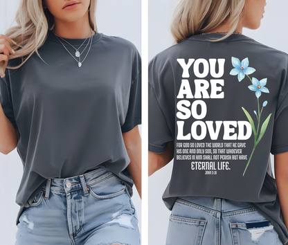 On the back of this Christian custom unisex t-shirt are the words You are loved in large bubble letters with a blue wildflower next to the words, the bible scripture John 3:16 is underneath that reads For God so loved the world that he gave his only son, so that whoever believes in him shall not perish but have everlasting life.