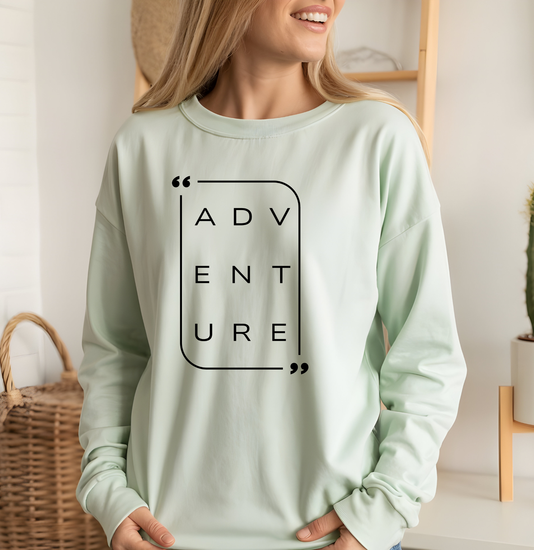 On the front of this super soft unisex long sleeve shirt is the word adventure with there being three letters on each line, it is in a modern font. There is a border around the word.