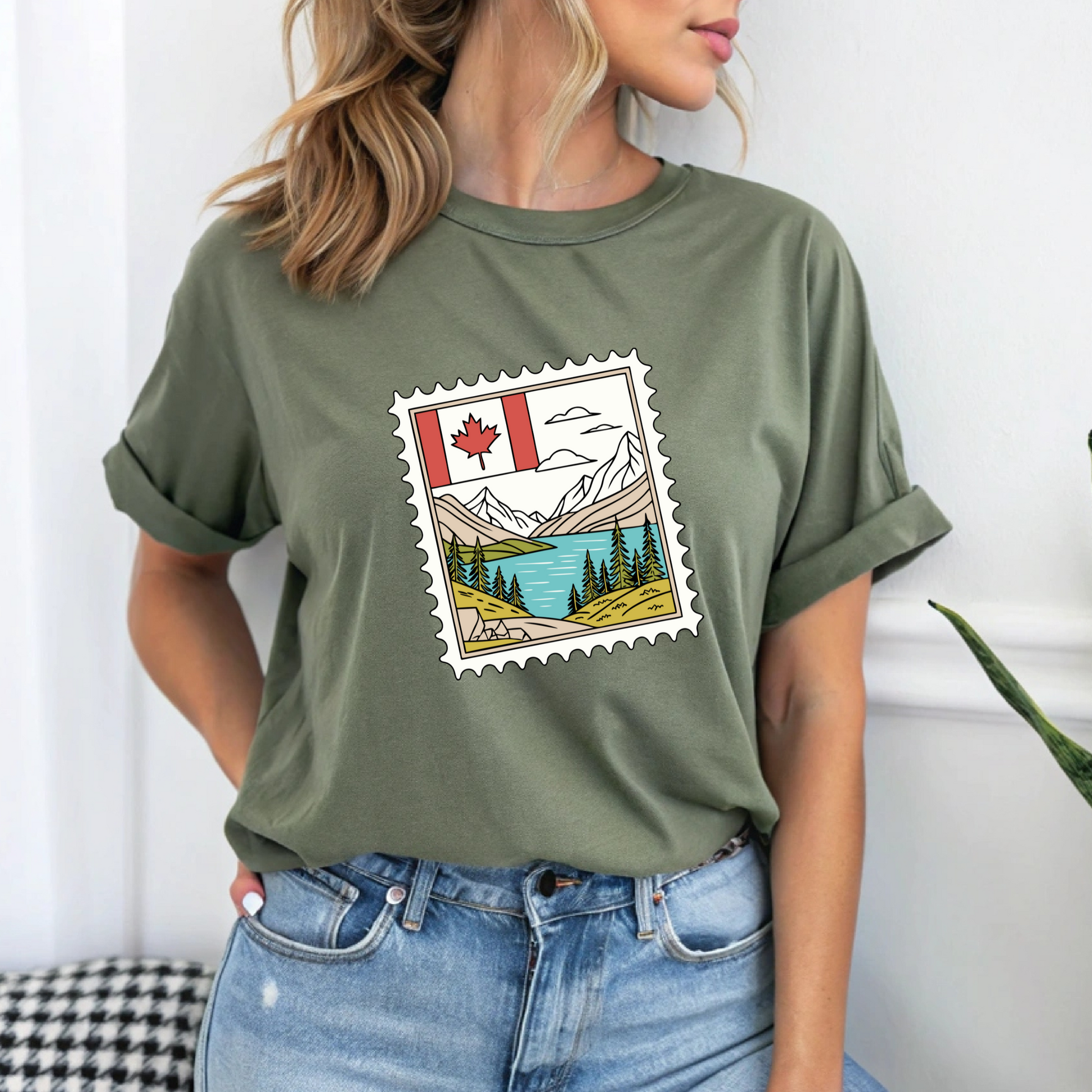 On the front of this custom Canadian pride short sleeve shirt is an image of a Canadian postage stamp with the Canadian flag in one corner and an image of mountains, a lake, and trees the make up the rest of the stamp.