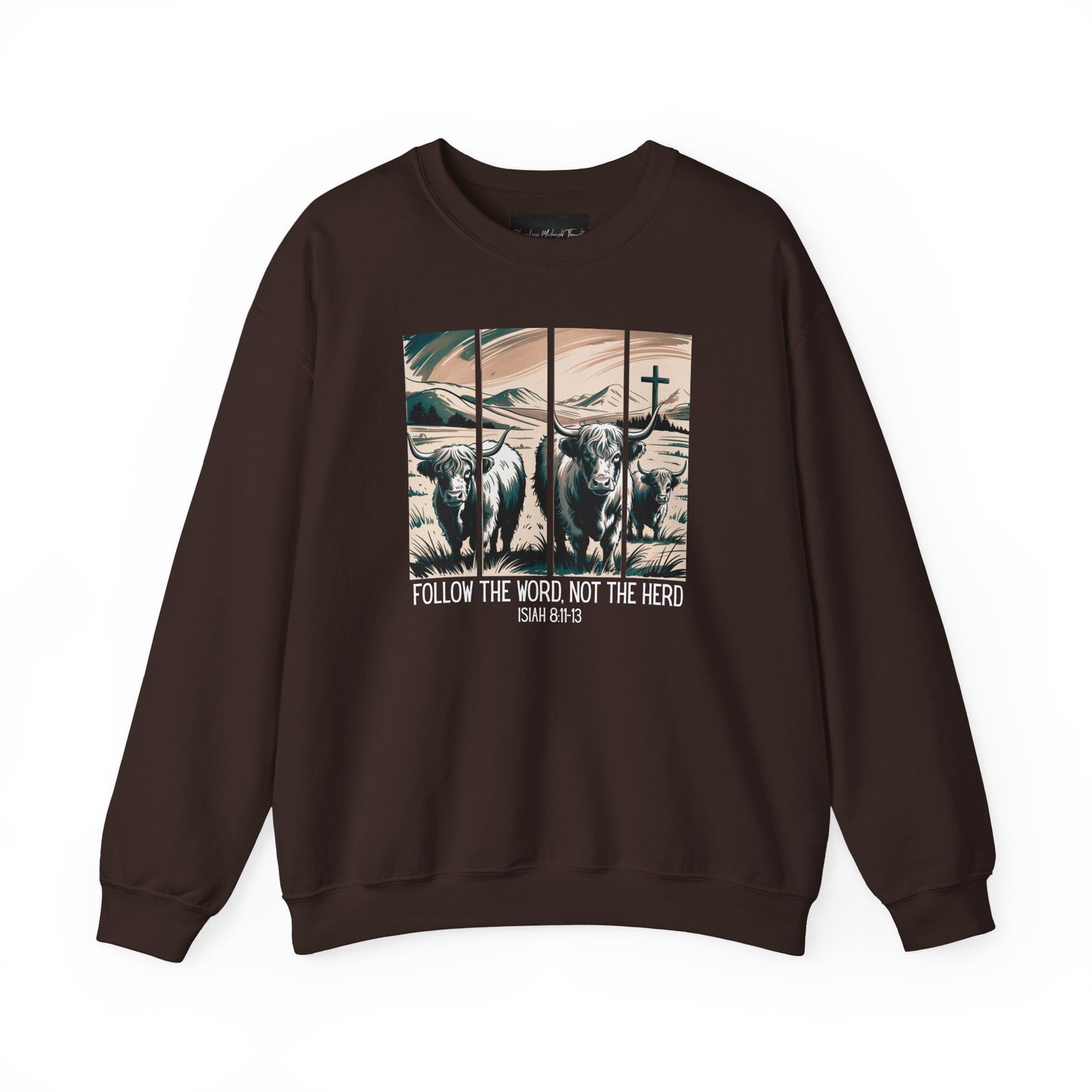 On the front of this Christian pullover sweatshirt is the image of cows standing in a pasture that is in a valley surrounded by mountains, there is a Jesus cross behind the cows, underneath the image is the scripture Follow the word, not the herd Isiah 8:11-13