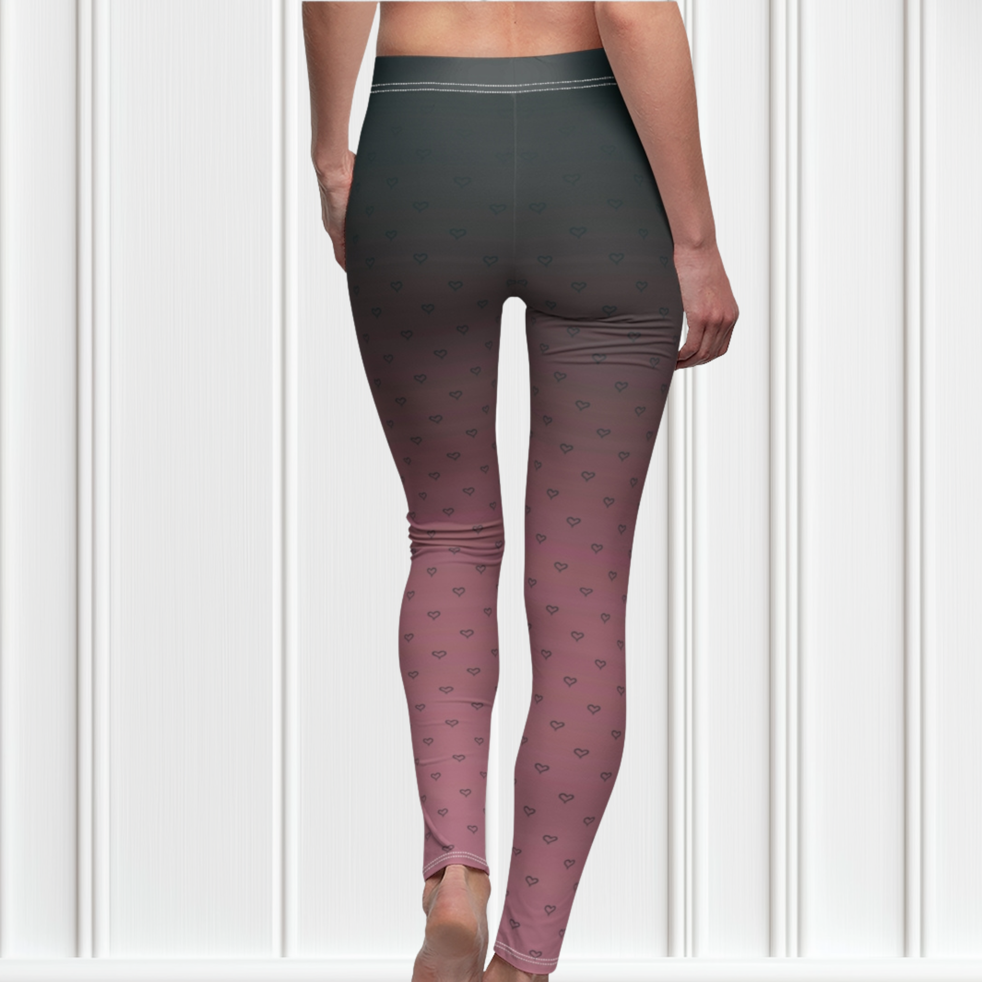 A pair of women's custom high waisted leggings that start as black at the top then fade to a light pink at the bottom, there are hearts all over the leggings then they fade into the black at the top of the pant.