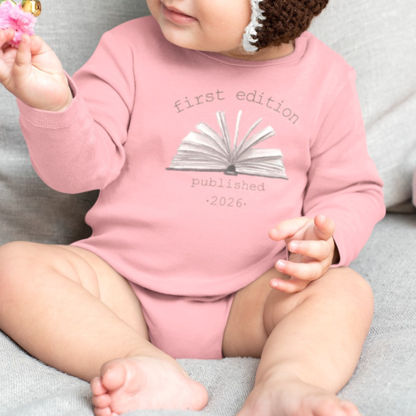 On the front of this custom baby onesie are the words First Edition Published 2026 with an image of an open book in the middle of the wording.