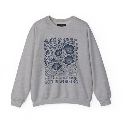 On the front of this custom women's Christian pullover sweatshirt are a bunch of wildflowers with the words in the waiting God is working underneath the flowers.