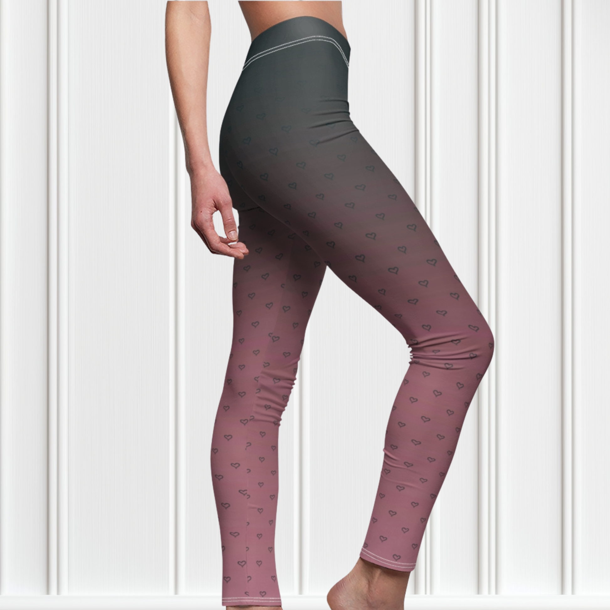 A pair of women's custom high waisted leggings that start as black at the top then fade to a light pink at the bottom, there are hearts all over the leggings then they fade into the black at the top of the pant.
