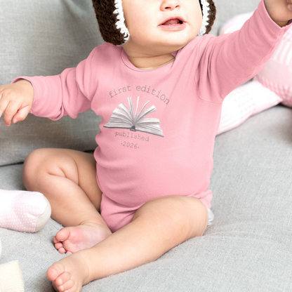 On the front of this custom baby onesie are the words First Edition Published 2026 with an image of an open book in the middle of the wording.