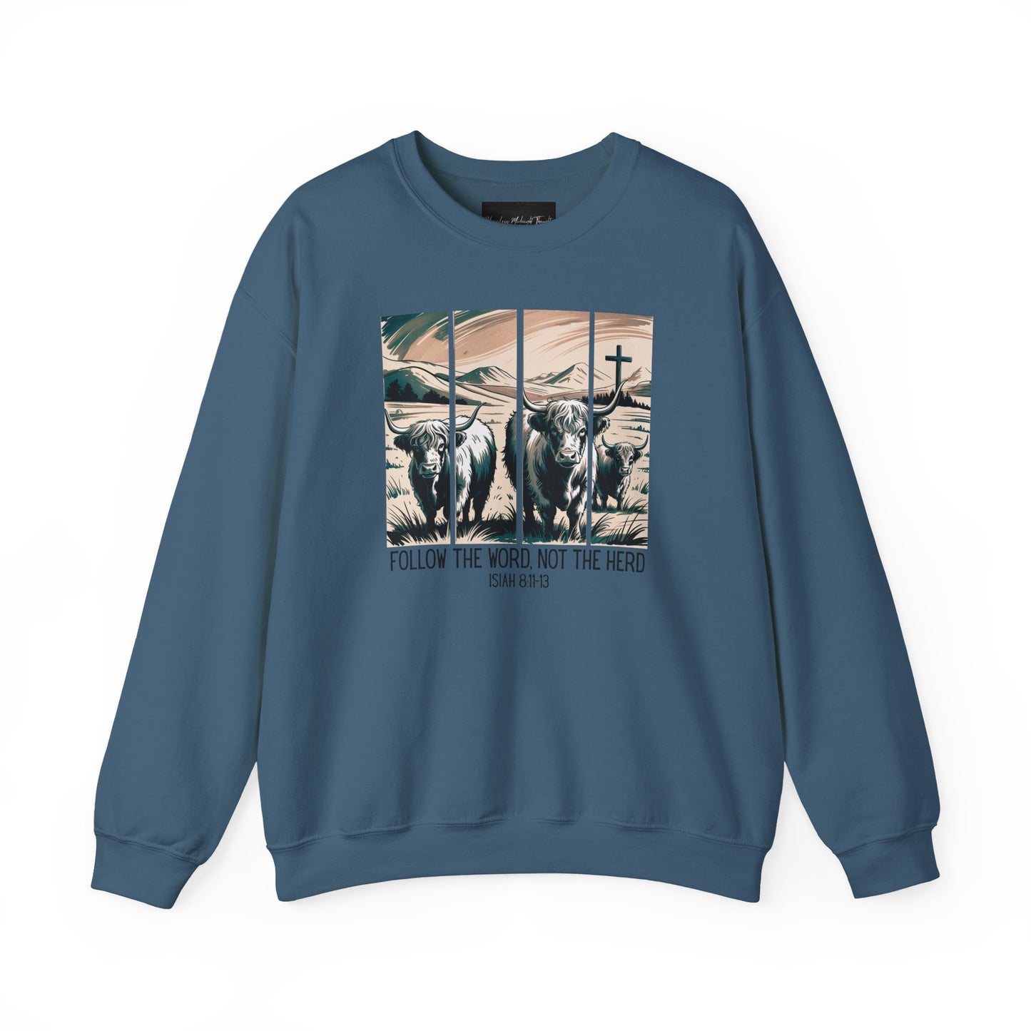 On the front of this Christian pullover sweatshirt is the image of cows standing in a pasture that is in a valley surrounded by mountains, there is a Jesus cross behind the cows, underneath the image is the scripture Follow the word, not the herd Isiah 8:11-13