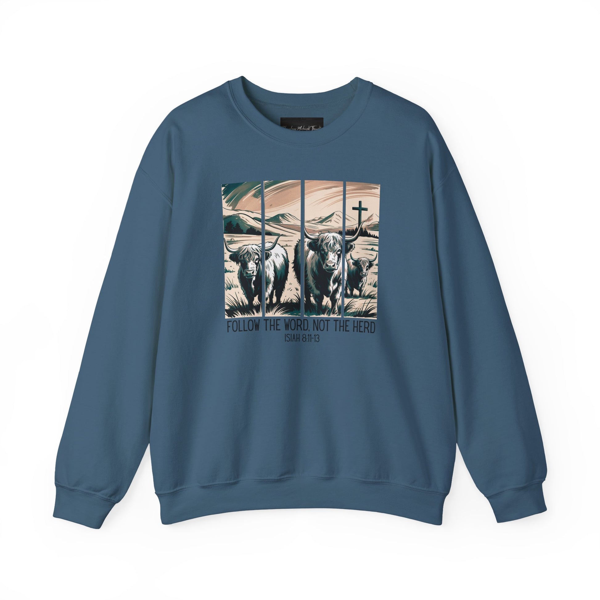 On the front of this Christian pullover sweatshirt is the image of cows standing in a pasture that is in a valley surrounded by mountains, there is a Jesus cross behind the cows, underneath the image is the scripture Follow the word, not the herd Isiah 8:11-13