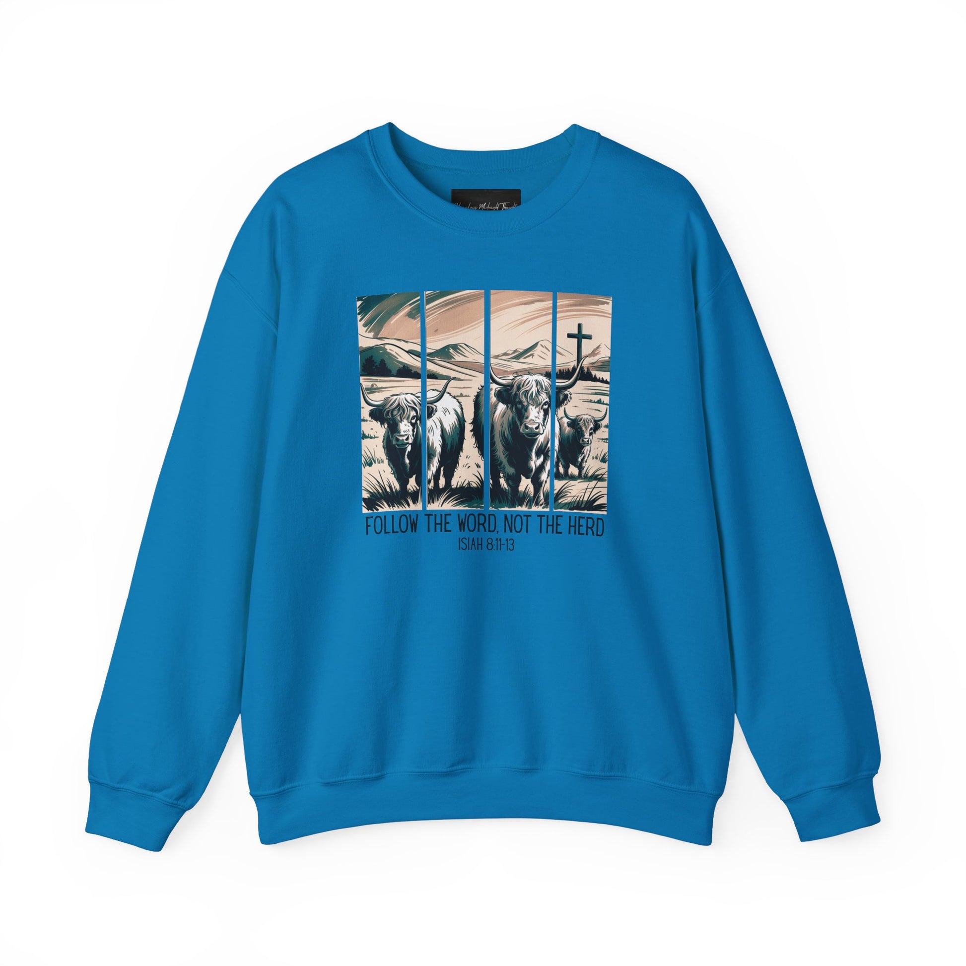 On the front of this Christian pullover sweatshirt is the image of cows standing in a pasture that is in a valley surrounded by mountains, there is a Jesus cross behind the cows, underneath the image is the scripture Follow the word, not the herd Isiah 8:11-13