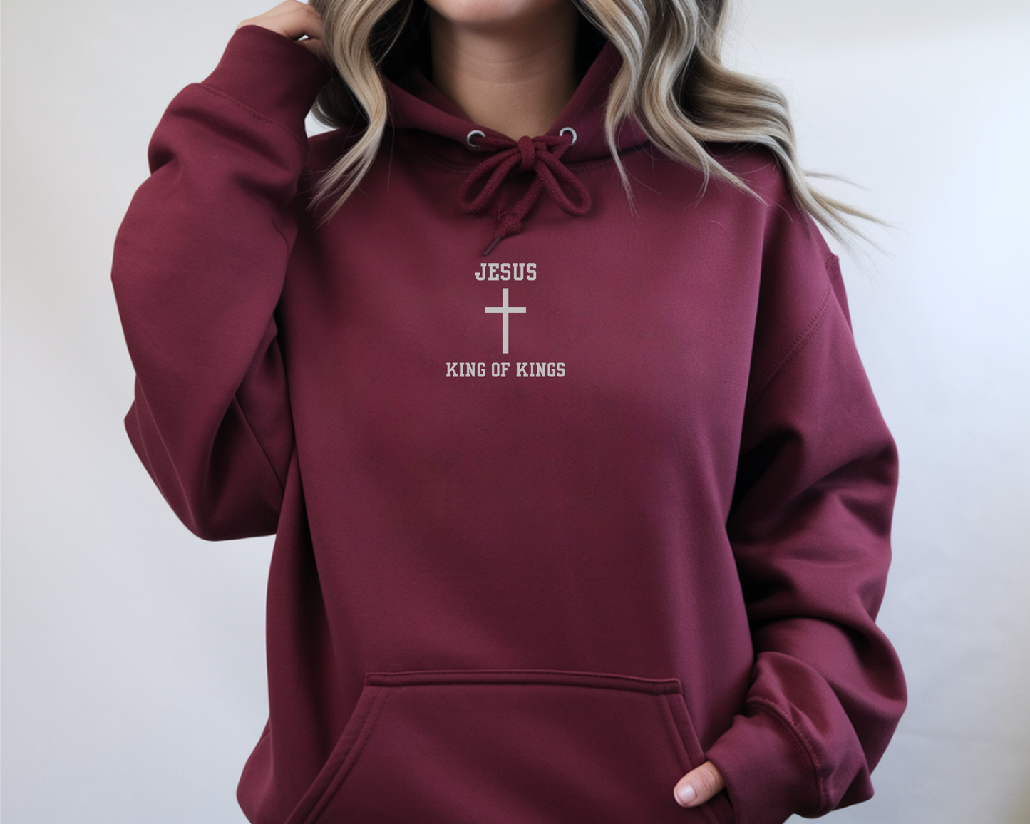 On the front of this custom embroidered unisex hooded sweatshirt are the words Jesus King of Kings with a Jesus cross in the center embroidered into the upper middle of the hoodie in silver thread.