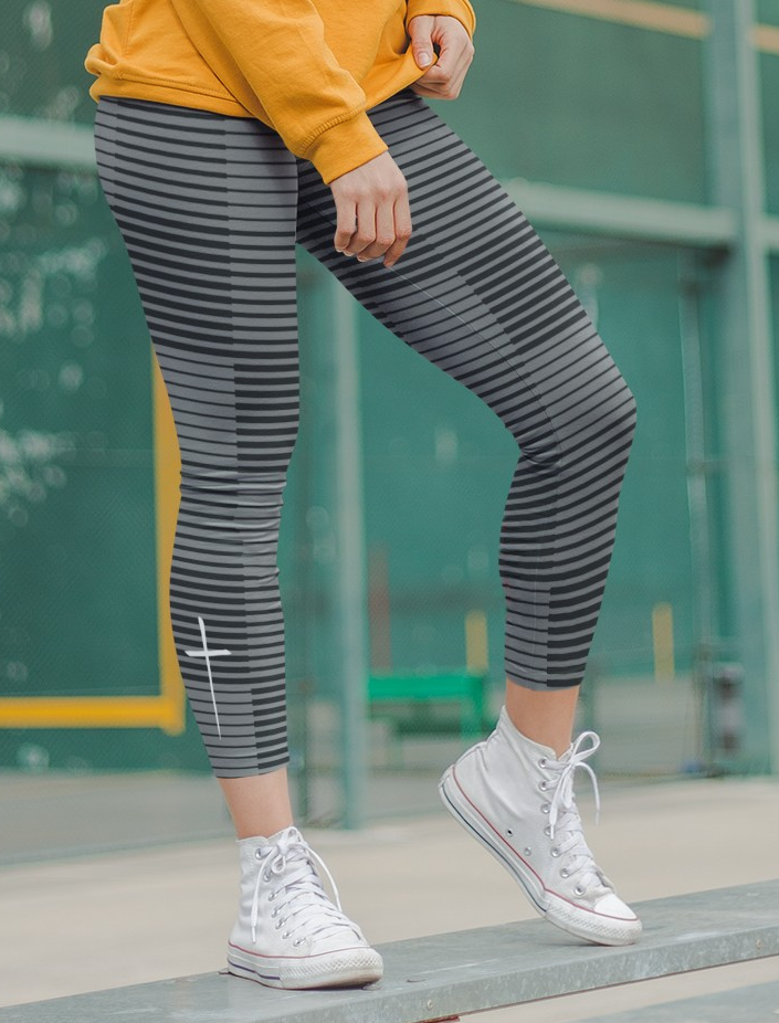 A pair of women's high waisted Christian themed leggings, the pants are light grey  color with black stripes running across the pants, the lines are in different thicknesses from the top to the bottom ankle of the leggings giving it a 3D look when worn, there is a white Jesus cross on the bottom right calf of the pant.