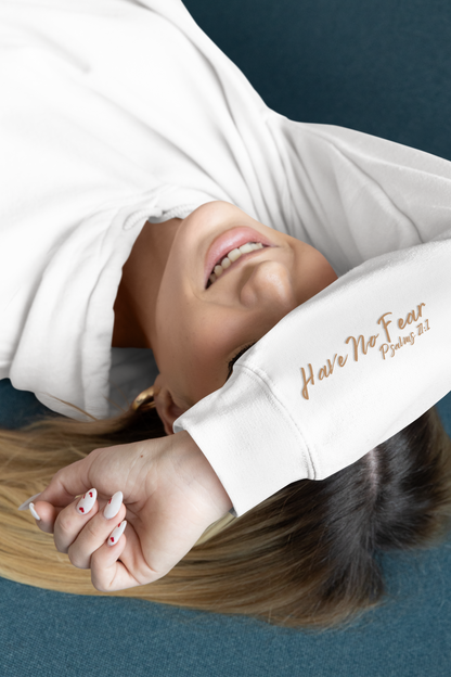 This custom Christian unisex hoodie features a image of a majestic male lion roaring with a Jesus cross overlayed overtop of the lion on the back of the hoodie, the bible verse Have No Fear Psalms 27:1 is on the right sleeve in gold cursive font.