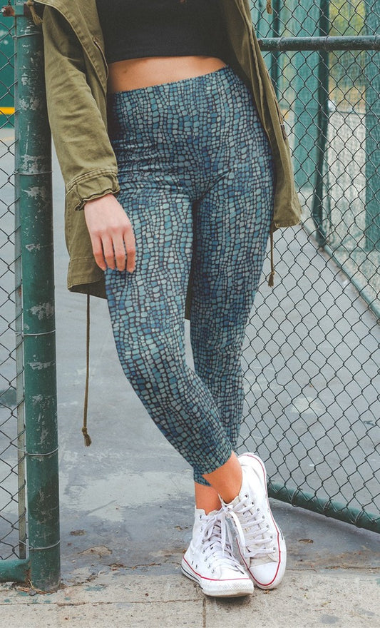 A pair of custom handmade high waisted women's leggings that have a emerald green and turquoise colored snake scale pattern all over the pants.