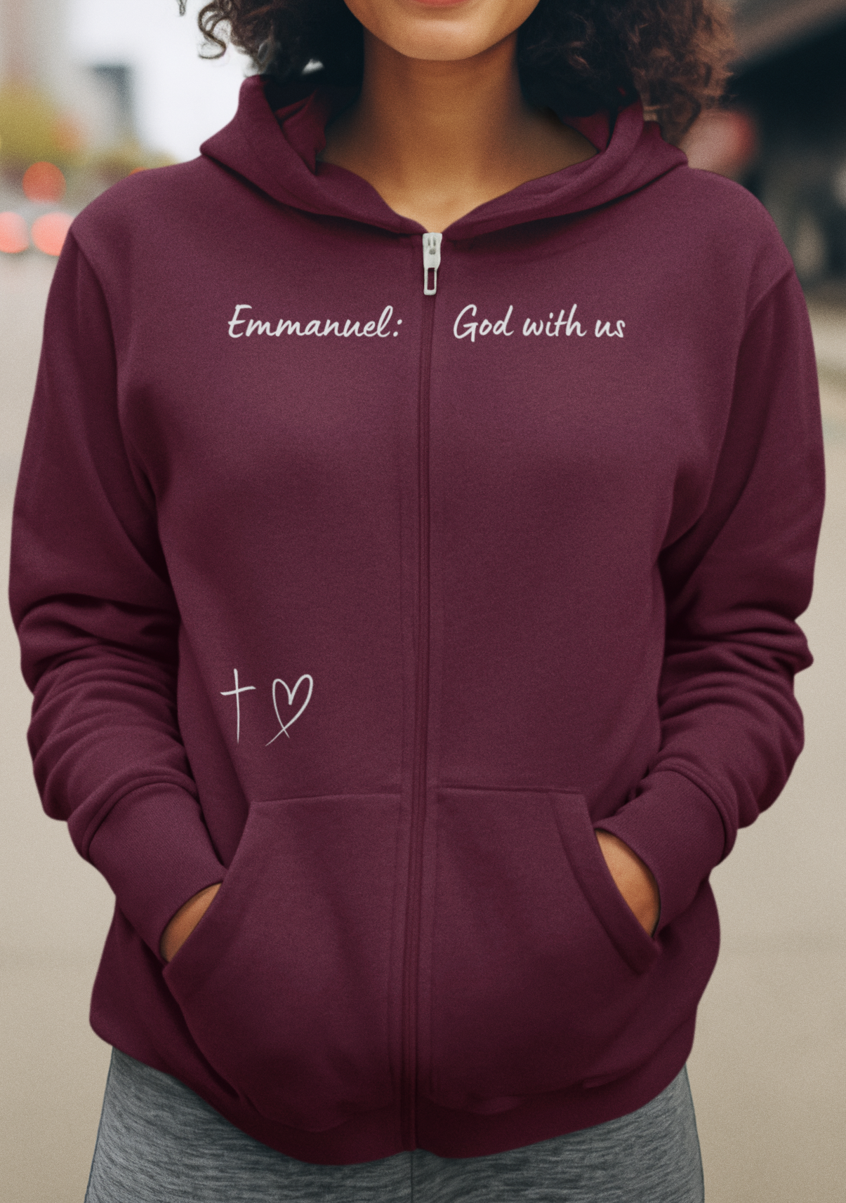 This Unisex Heavy Blend™ Full Zip Hooded Sweatshirt features the words Emmanuel God With Us on the upper chest and an image of a cross with a heart above the pocket.
