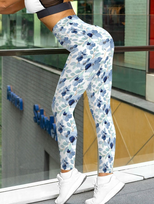 A pair of custom handmade high waisted women's leggings that are white and have a blue floral pattern with green leaves all over the pants.