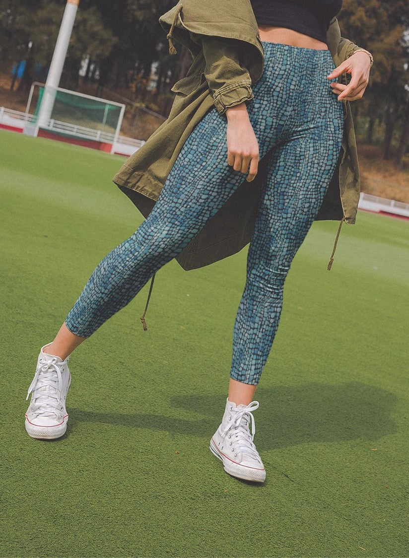 A pair of custom handmade high waisted women's leggings that have a emerald green and turquoise colored snake scale pattern all over the pants.