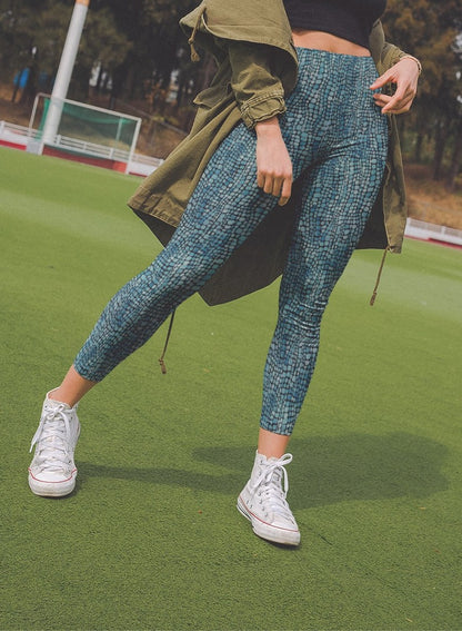 A pair of custom handmade high waisted women's leggings that have a emerald green and turquoise colored snake scale pattern all over the pants.