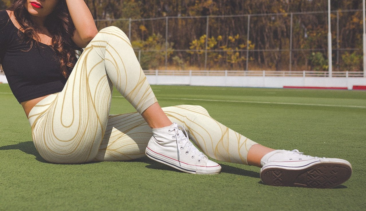 These custom women's high waisted leggings have a base color of a light beige  that fades to a even brighter beige at points to give off a 3D wave design, there are gold lines overlayed across the top of the beige that contour to the body.