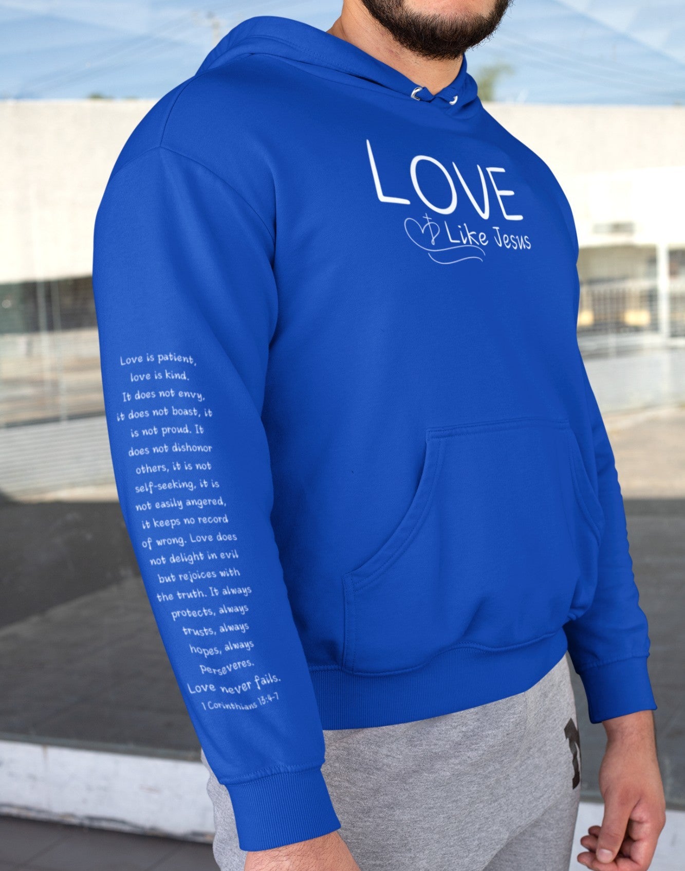 A cozy and warm custom Christian hoodie featuring a powerful message of love and faith. The front displays the word LOVE Like Jesus, accompanied by a cross with a heart. Each sleeve showcases the scripture 1 Corinthians 13:4-7