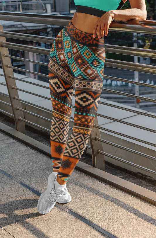 A pair of super soft handmade women's ankle length high waisted leggings. The pattern throughout the entire pair of pants is a orange, brown and blue Aztec pattern from the top of the pants to the bottom of the leggings.