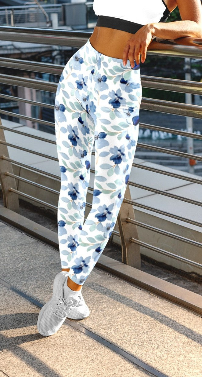 A pair of custom handmade high waisted women's leggings that are white and have a blue floral pattern with green leaves all over the pants.