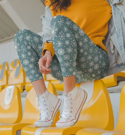 A pair of high waisted custom women's leggings that are a light blue in color and have white snowflakes all over the pants, perfect for Christmas.