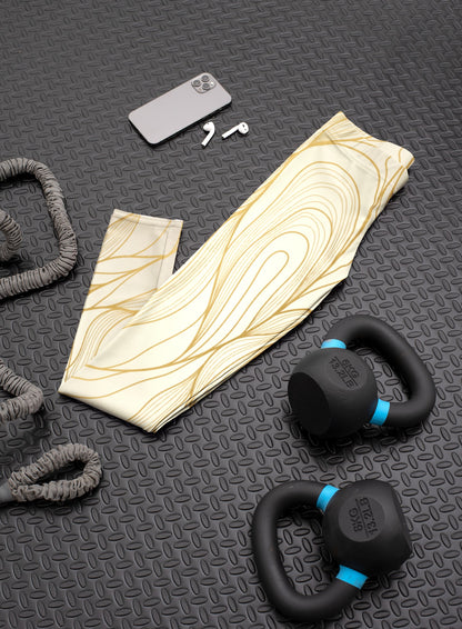 These custom women's high waisted leggings have a base color of a light beige  that fades to a even brighter beige at points to give off a 3D wave design, there are gold lines overlayed across the top of the beige that contour to the body.