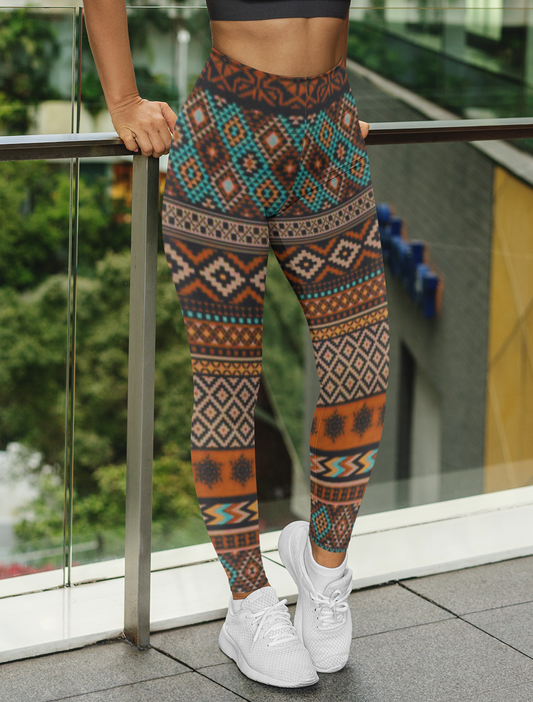 A pair of super soft handmade women's ankle length high waisted leggings. The pattern throughout the entire pair of pants is a orange, brown and blue Aztec pattern from the top of the pants to the bottom of the leggings.