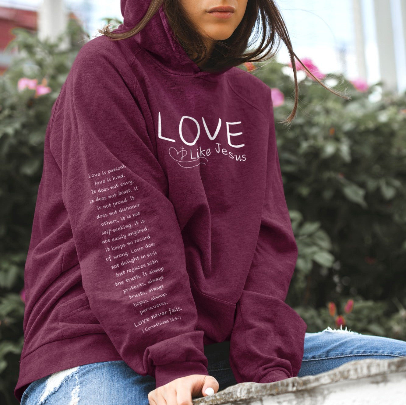 A cozy and warm custom Christian hoodie featuring a powerful message of love and faith. The front displays the word LOVE Like Jesus, accompanied by a cross with a heart. Each sleeve showcases the scripture 1 Corinthians 13:4-7