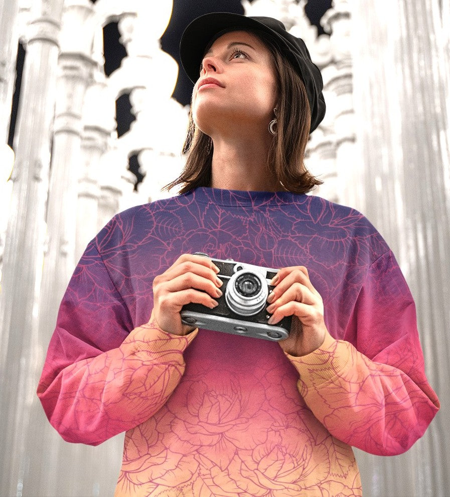 The sweater has a washed ombre pattern starting as a dark purple at the top of the neckline then fading to a light purple then to a bright pink then to a blush pink at the bottom, there is a purple floral pattern imposed on the top of the sweater.