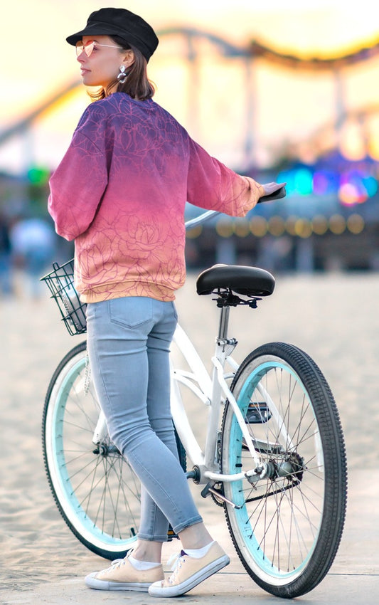 The sweater has a washed ombre pattern starting as a dark purple at the top of the neckline then fading to a light purple then to a bright pink then to a blush pink at the bottom, there is a purple floral pattern imposed on the top of the sweater.
