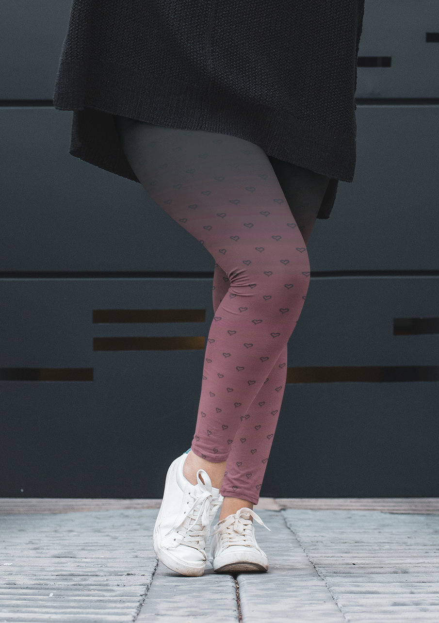 A pair of women's custom high waisted leggings that start as black at the top then fade to a light pink at the bottom, there are hearts all over the leggings then they fade into the black at the top of the pant.