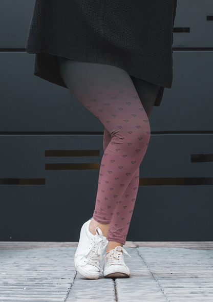 A pair of women's custom high waisted leggings that start as black at the top then fade to a light pink at the bottom, there are hearts all over the leggings then they fade into the black at the top of the pant.