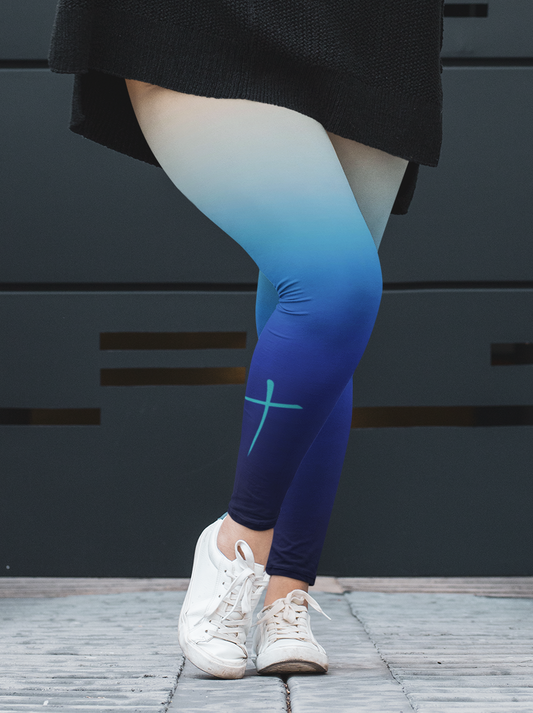 A pair custom handmade high waisted women's ombre leggings, the top of the leggings starts as a orange then it fades to a light blue then to a turquoise blue then finally a navy blue at the ankle, there is a turquoise blue Jesus cross on the right calf of the pant.